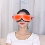A woman wearing a red eye massager and a white t-shirt sitting on a beige sofa in front of white curtains.