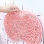 A pink silicone scrubber pad with dense white bristles, held by a hand against a white tiled wall.