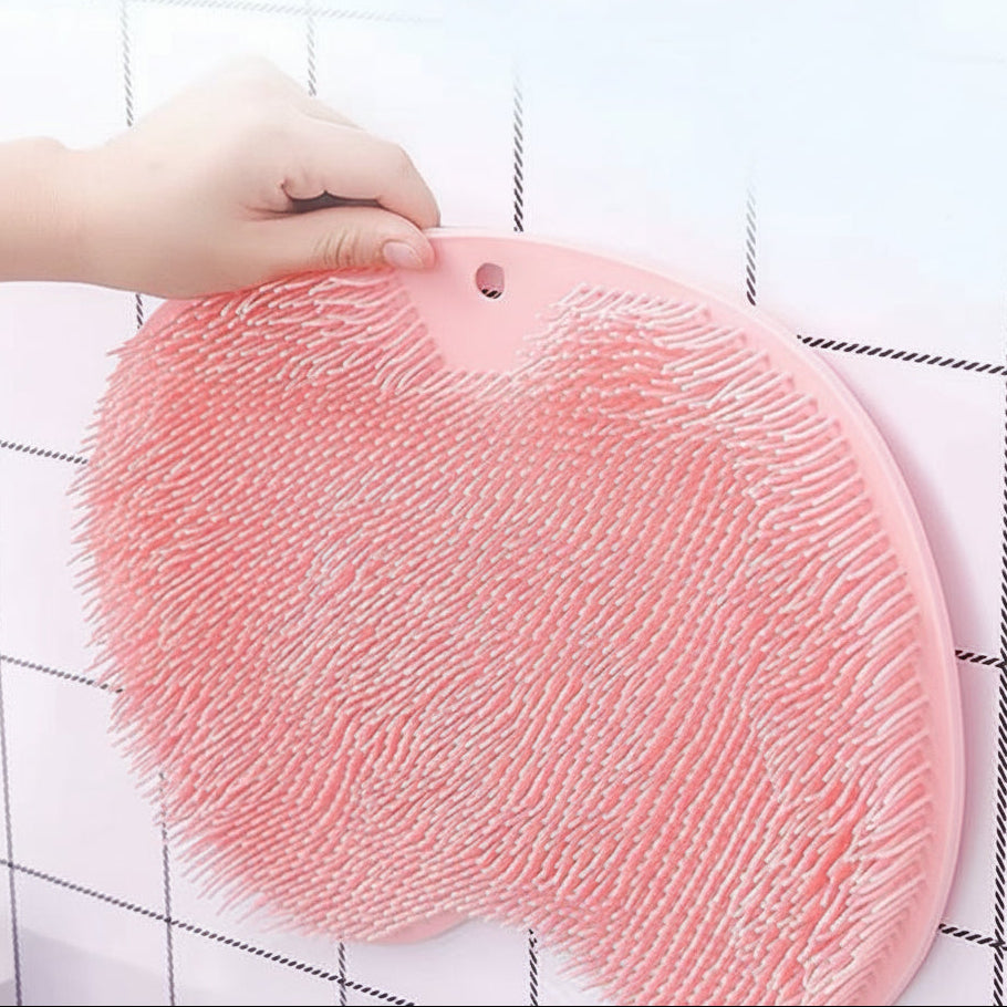 A pink silicone scrubber pad with dense white bristles, held by a hand against a white tiled wall.