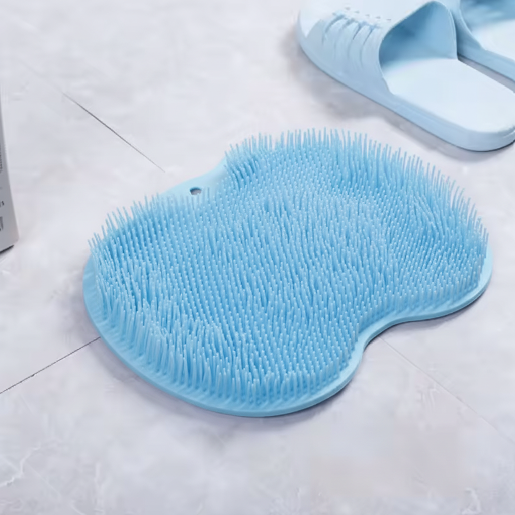 A light blue silicone scrubber pad with dense bristles on a light gray tiled floor, with a pair of matching light blue slippers partially visible in the background.
